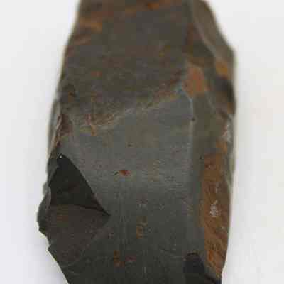 Lengthwise view of basalt adze (ko'i): The image shows a weathered, ancient stone adze (ko'i) with a dark, roughly hewn surface, showcasing signs of use and age, possibly employed for carving.