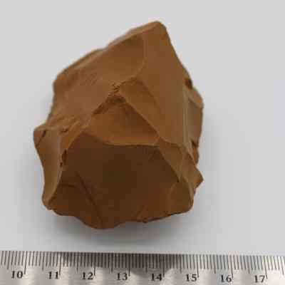 Adze preform with ruler: The image shows a rough-textured brown stone, resembling an adze preform, next to a metric ruler on a plain background.