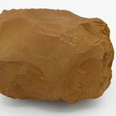 Closeup of adze preform: The image shows a roughly shaped, brown stone adze preform, displaying various chipped surfaces for further refinement.