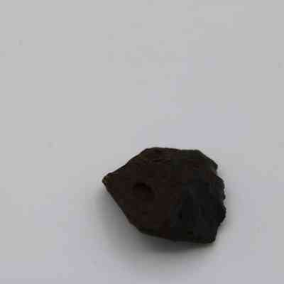 Closeup of glass flake: A small, dark glass flake rests on a plain, light surface, showcasing its textured and uneven edges.