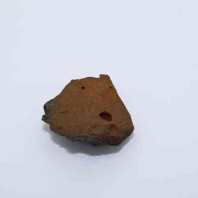 Closeup of glass flake: A fragment of glass flake, characterized by its rough, rust-colored surface and irregular edges, lies on a smooth, white background.