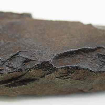 Closeup profile of an adze fragment: The image shows a dark, irregularly shaped basalt adze with a polished edges.