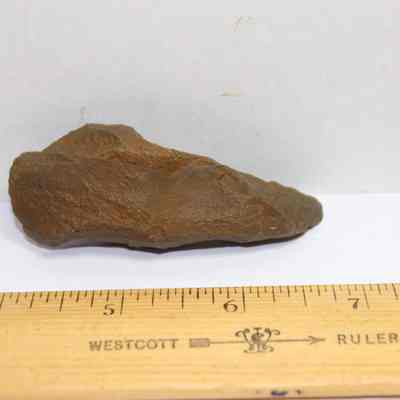 Basalt awl and ruler: A brown rock is positioned next to a ruler, measuring around six inches long, on a plain white background.