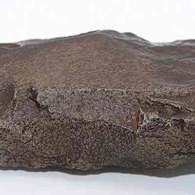 Profile of an adze fragment: The image shows an uneven, dark brown basalt adze fragment with a jagged surface, lying against a plain white background.
