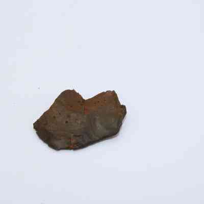 Closeup basaltic glass flake: A rough-textured basaltic glass flake with a dark, earthy hue lies against a plain white background.