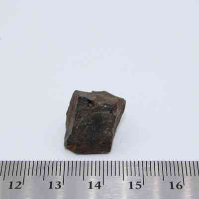 Glass core with ruler: A small, angular piece of glass core lies near a ruler, showcasing its rough, jagged surface and dark color amidst a plain background.