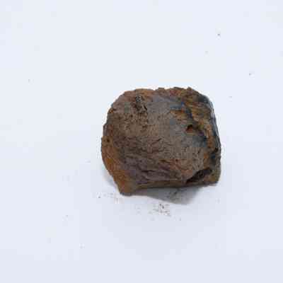 Closeup of basaltic glass core: The image shows a small piece of basaltic glass core with rough, uneven texture and dark brown color resting on a white surface.