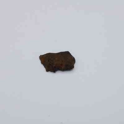 Closeup of basaltic glass flake: A small, rough-textured flake of basaltic glass rests on a smooth white surface, displaying its dark, earthy coloration distinctively.