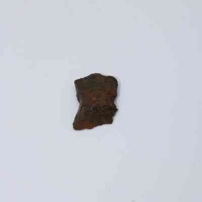 Closeup of basaltic glass flake: The image shows a small, textured basaltic glass flake on a plain white background, highlighting its rough surface and dark coloration.