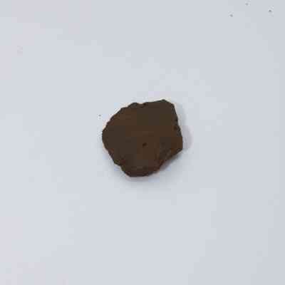 Small basaltic glass flake: A dark, irregularly shaped piece of basaltic glass flake sits on a plain white background, highlighting its rough texture and earthy color.