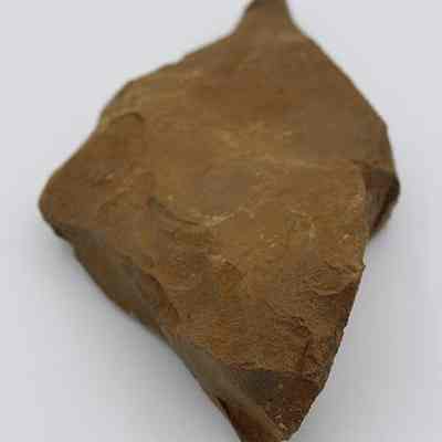 Lengthwise view of basalt drill: The image shows a piece of brown rock drill with a rough, jagged surface, featuring various shades and textures, against a plain, white background.