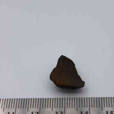 Closeup of basaltic glass core with ruler: The image depicts a small piece of basaltic glass next to a ruler, highlighting its black, porous texture.