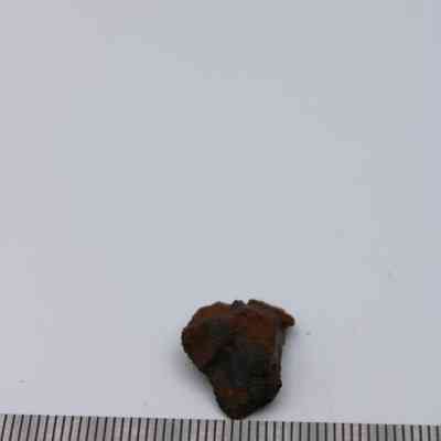 Closeup of basaltic glass core with ruler: A small piece of basaltic glass core rests on a white surface, with a ruler indicating its size and scale in the foreground.