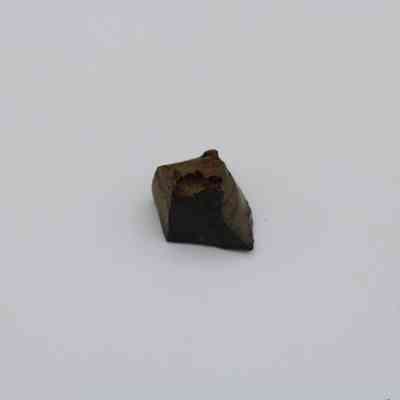 Closeup of basaltic glass core: The image shows a small, angular piece of basaltic glass core, characterized by a dark, glossy surface and some rough, textured areas.