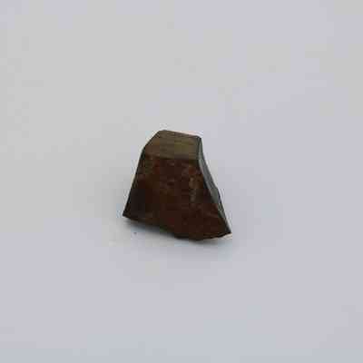 Close up of basaltic glass core: The image shows a small, angular basaltic glass core with a rough, dark surface, positioned against a plain, light background.
