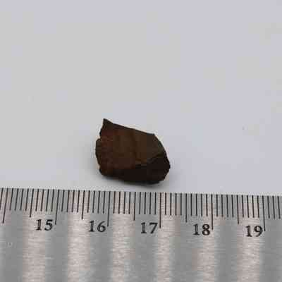 Basaltic glass core and metal ruler: The image shows a small piece of basaltic glass core placed against a ruler for scale measurement on a white background.