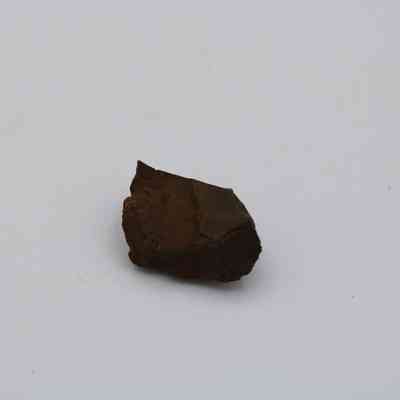 Closeup of basaltic glass core: The image displays a small, dark piece of basaltic glass core against a plain white background, highlighting its rough, matte texture.