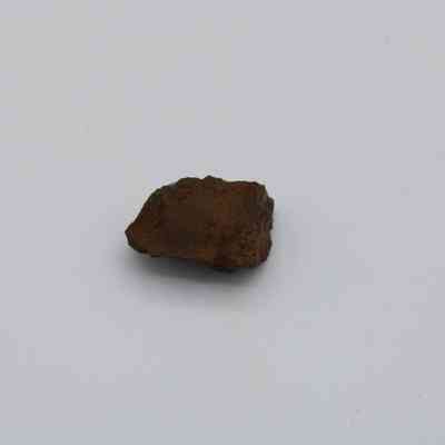 Closeup of basaltic glass core: The image shows a small piece of basaltic glass core, characterized by its dark, rough texture, and exhibited against a plain light background.