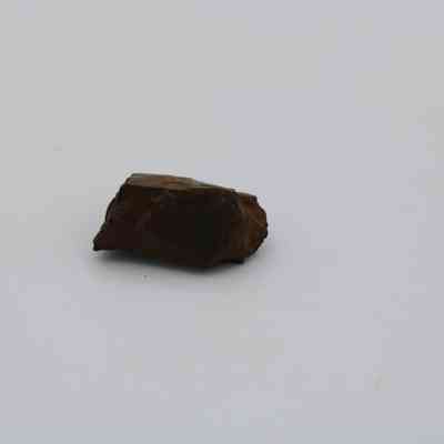 Closeup of basaltic glass core: A small piece of basaltic glass core rests against a plain, light background, showcasing its natural dark brown hue.