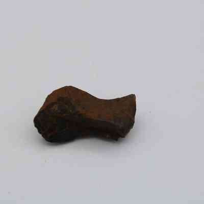 Closeup of a basaltic glass pāhoehoe core: The image shows a small, dark brown piece of pāhoehoe lava with a smooth, ropy texture against a plain background.