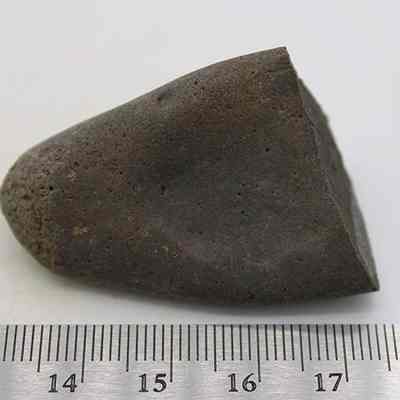 Side profile of hammerstone with ruler: The image shows a dark, triangular rock placed next to a ruler for scale, measuring approximately 5 centimeters in length.
