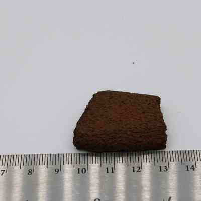File fragment and metal ruler: A small, textured fragment of basalt is placed on a flat surface next to a metal ruler displaying measurements in centimeters.