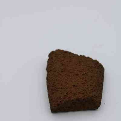 Closeup of basaltic file fragment: The image shows a dark, porous fragment of basaltic glass, displaying a rough texture, set against a plain, light background.