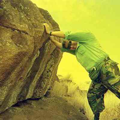 Derek Chow leaning on large pohaku (stone)