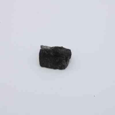 Closeup of basaltic glass flake: The image shows a small, dark basaltic glass flake against a plain, white background, highlighting its rough texture and solid surface.