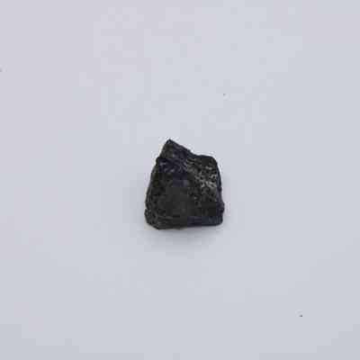 Closeup of basaltic glass flake: A black basaltic glass flake sits on a plain white background, showcasing its rough texture and irregular shape.