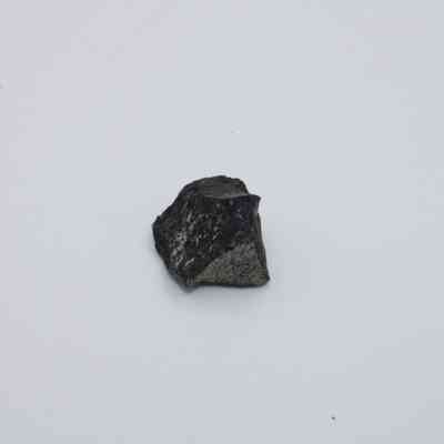 Basaltic glass flake: The image shows a small, irregularly shaped basaltic glass flake with dark, glossy surfaces, resting on a plain white background.
