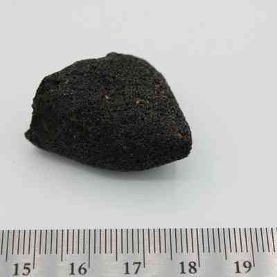 Basaltic glass core with ruler: A small, dark, rough-textured basaltic glass core rests against a white background with rulers for size reference.