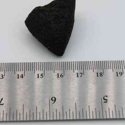 Closeup of basaltic glass core with ruler: The image shows a basaltic glass core placed beside a metal ruler, displaying its size and rugged texture.
