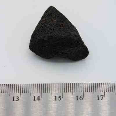 Closeup of basaltic glass core with ruler: The image shows a small, dark basaltic glass core positioned above a ruler for scale reference.