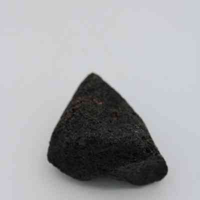 Closeup of basaltic glass core: The image shows a dark, textured piece of basaltic glass core resting on a plain, light-colored surface.