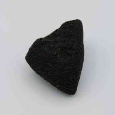 Closeup of basaltic glass core: The image shows a dark, rough-textured piece of basaltic glass core resting on a light surface, highlighting its natural formation and volcanic origin.