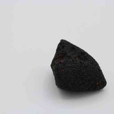 Basaltic glass core: The image shows a piece of basaltic glass core, with a dark, rough texture, resting on a plain, light background.