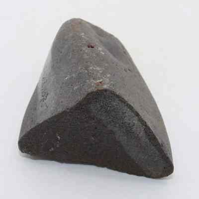 Closeup of triangular hammerstone: A roughly triangled shape dark stone with smooth edges is placed on a plain light background, showcasing its textured surface.