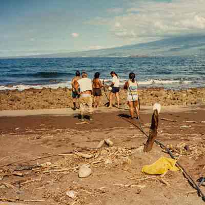 Group of people uncoiling black hose on beach
