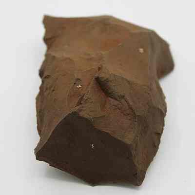 Lengthwise view of adze blank: The image shows a roughly hewn, angular brown stone tool with sharp edges resting on a plain white background.
