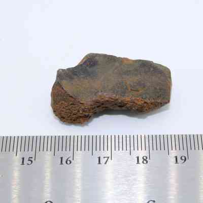 Closeup of glass flake with ruler: The image shows a small, jagged glass flake with a textured surface, placed beside a metal ruler measuring in centimeters.