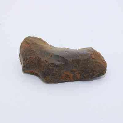 Closeup of glass flake: A rough, angular piece resembling a glass flake sits on a plain white surface, displaying varied textures and earthy colors.