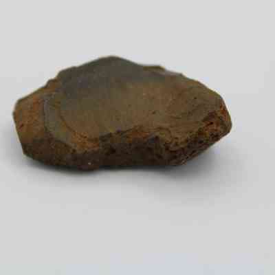 Closeup of glass flake: The image shows a rough, irregularly shaped glass flake with a brownish surface texture, resting on a plain white background.