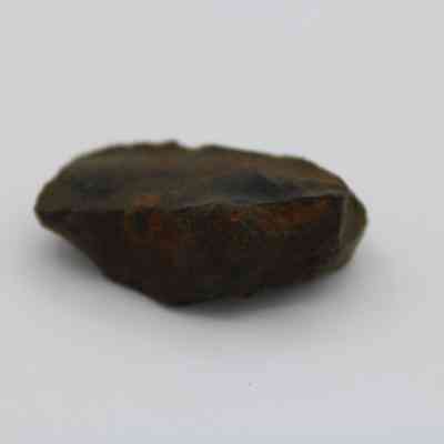 Closeup of glass flake: A brown, irregularly shaped glass flake rests on a plain white background, showcasing rough, natural edges in soft focus.