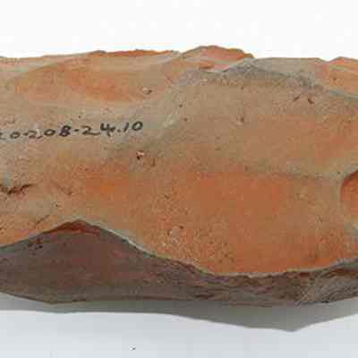Adze blank with visible alternate id number: The image shows a reddish-brown stone tool with visible flake scars, showcasing an ancient adze blank. Numbers are inscribed on its surface.