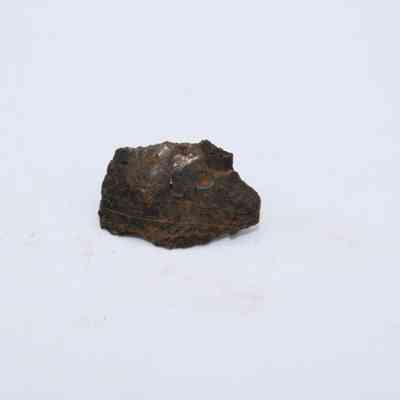 Closeup of basaltic glass flake: A small, rough-edged basaltic glass flake sits isolated on a plain, light-colored surface, showcasing its dark brown and slightly glossy texture.