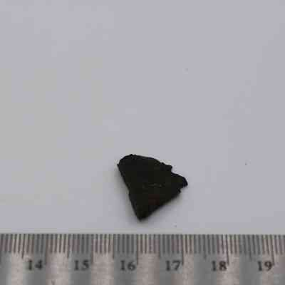 Basaltic glass with ruler: The image shows a small, dark fragment of basaltic glass placed on a white surface with a ruler indicating its size.