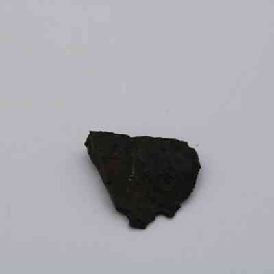 Closeup of basaltic glass: A small, dark piece of basaltic glass is positioned against a plain, light background, highlighting its irregular shape and rough texture.