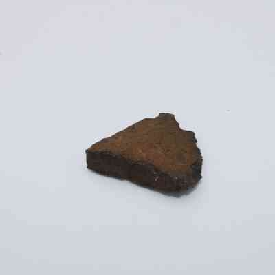 Triangular piece of basaltic glass: The image shows a piece of dark, rough-textured basaltic glass set against a plain white background, highlighting its rugged edges and earthy tone.