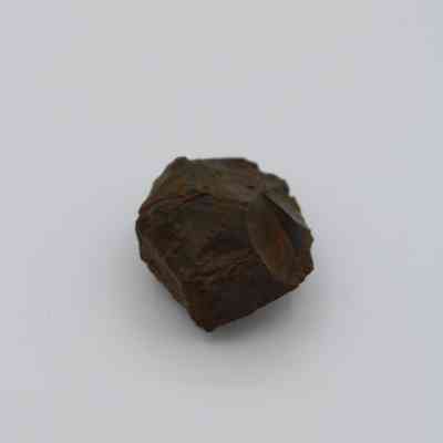 Closeup of basaltic glass core: The image shows a rough, dark-colored basaltic glass core resting on a plain, light background, highlighting its rugged texture and irregular shape.